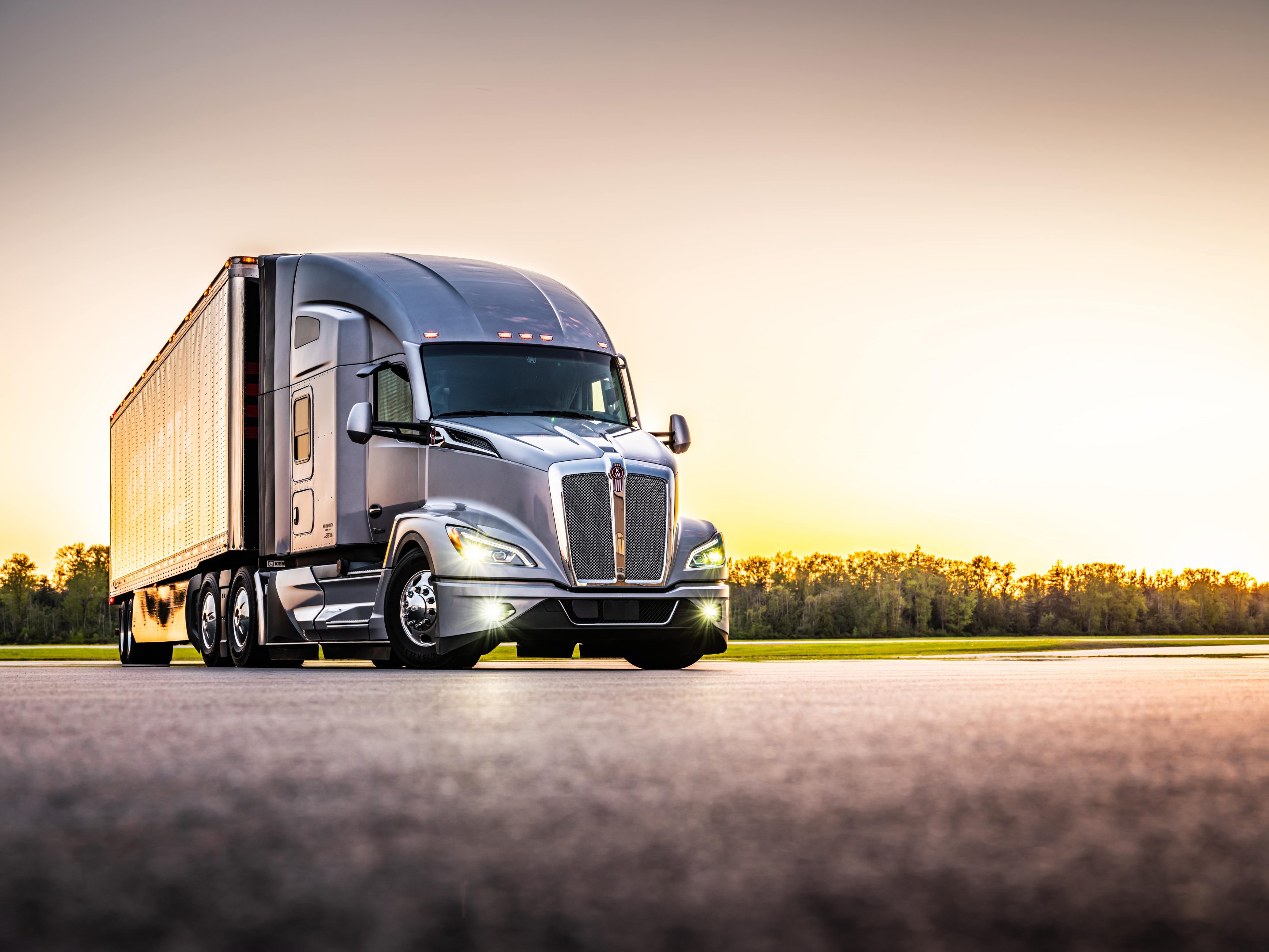 A grey Kenworth truck parked infront of a glowing sunset